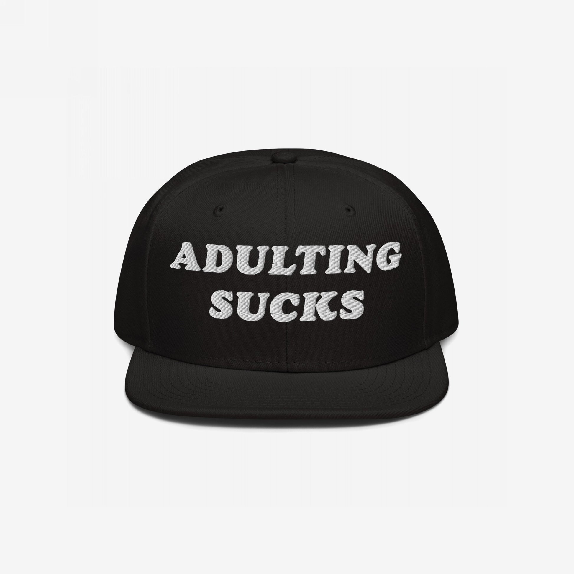 Black flat-brim snapback hat with ADULTING SUCKS embroidered in bold white letters, reflecting a candid, humorous take on life's challenges. Perfect for expressing shared frustrations while supporting a meaningful cause.