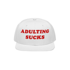 White flat-brim cap with bold red ADULTING SUCKS embroidery, reflecting a vintage-inspired, relatable style for expressing fr