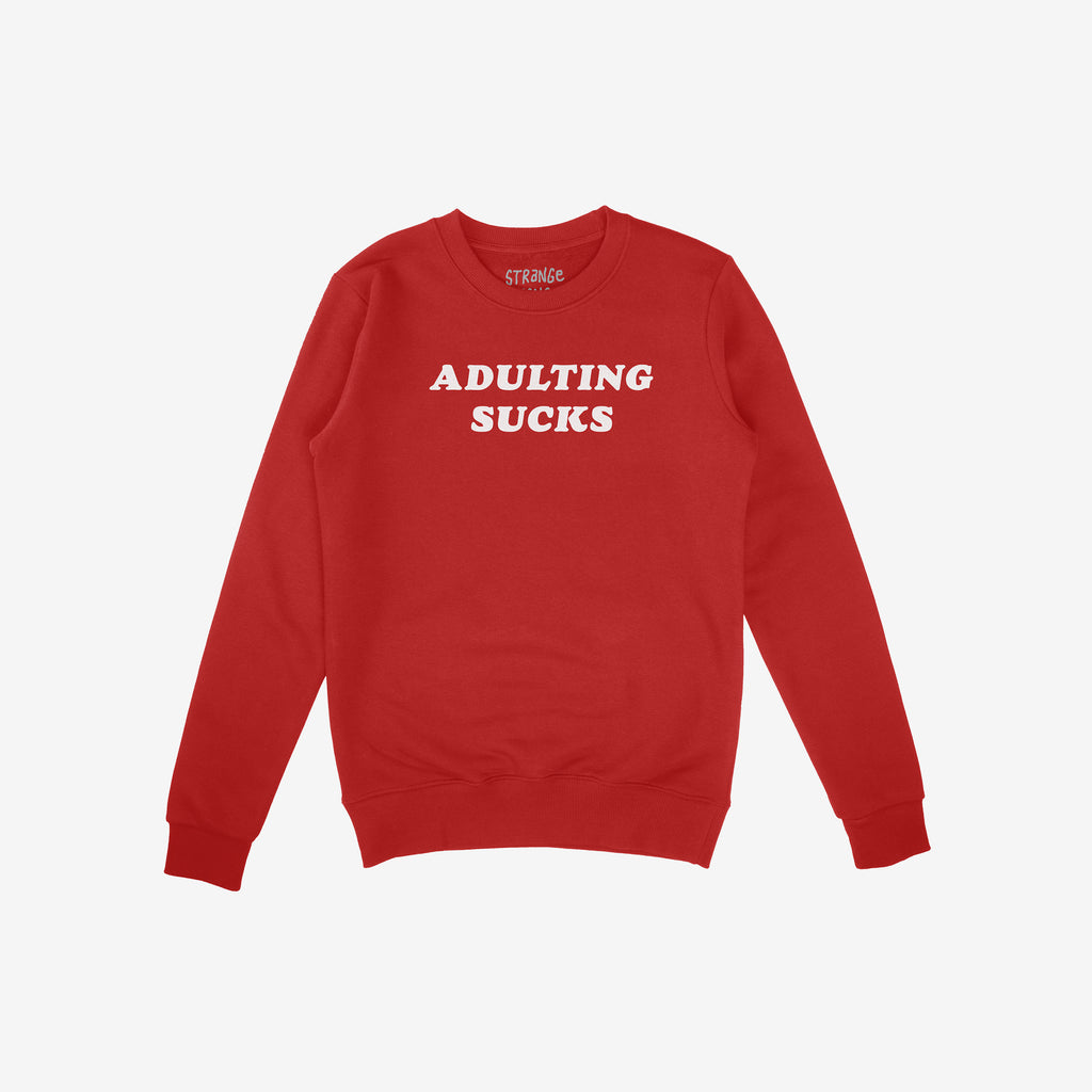 Red crewneck sweatshirt featuring the bold slogan “ADULTING SUCKS” in white, embodying a humorous take on the challenges of adulthood and aligning with a message of self-expression and individuality.