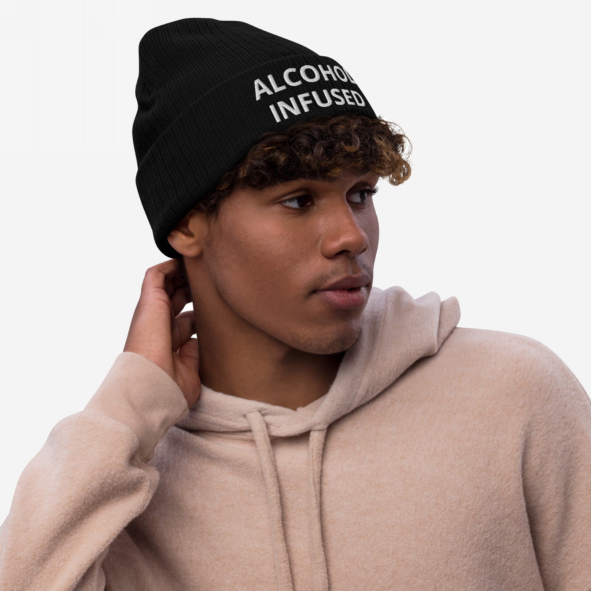 Young man in a black “Alcohol Infused” beanie, showcasing a light beige fleece hoodie, embodying a casual yet bold style with a touch of humor and rebellious spirit.