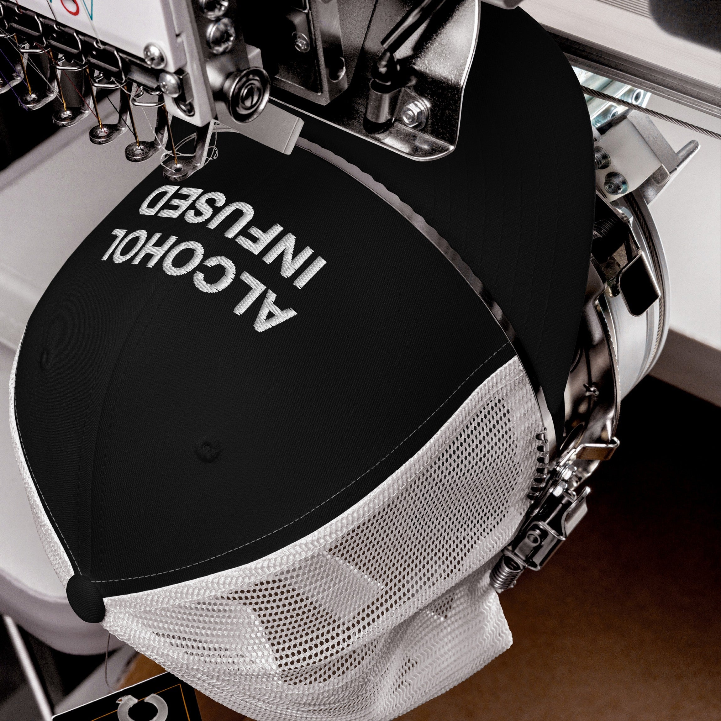 Embroidery machine stitching ALCOHOL INFUSED on a black and white trucker hat, symbolizing bold, irreverent style, perfect for making a statement at social gatherings.