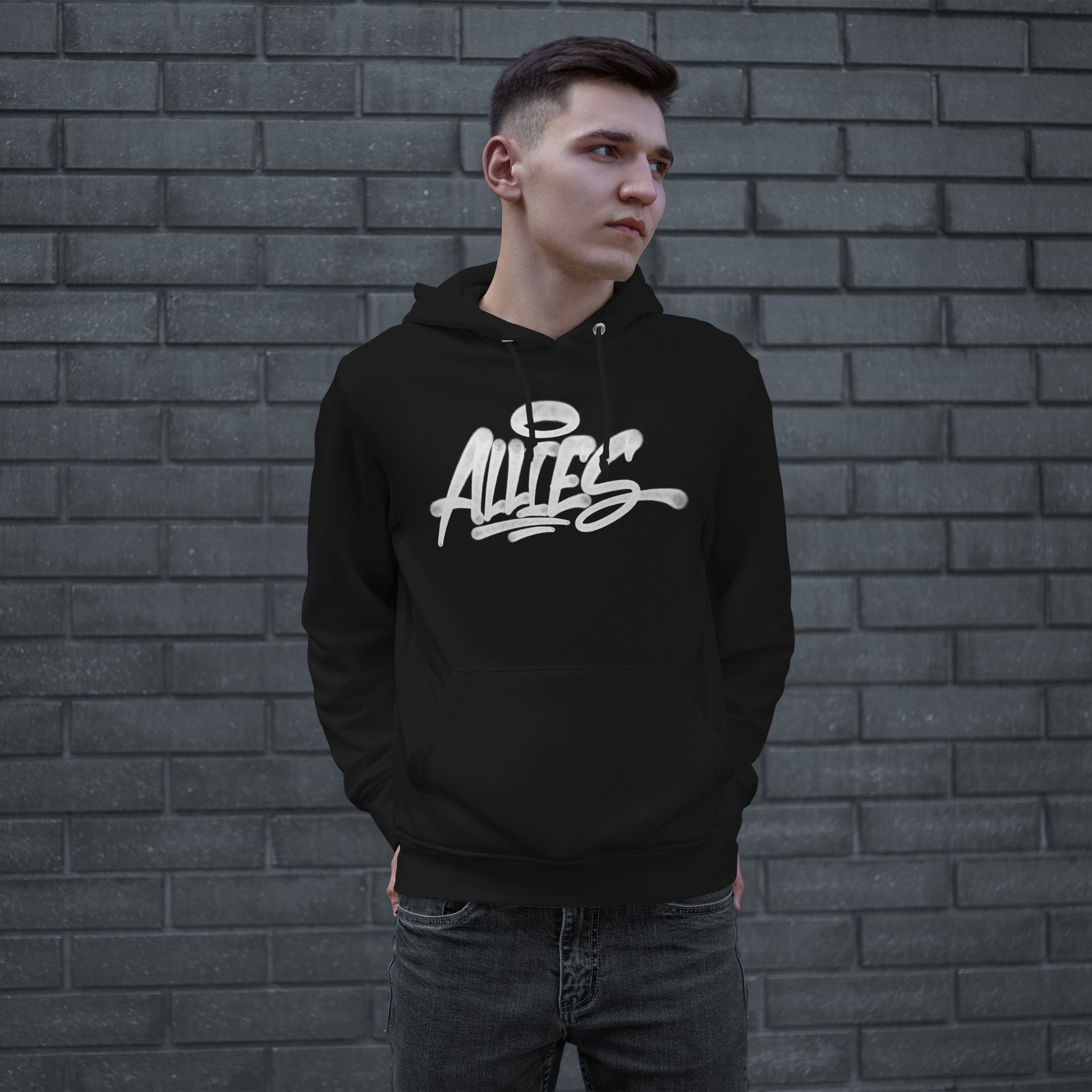 Young man wearing the Allies Handstyle Hoodie, featuring bold, graffiti-style script across the chest, embodying a statement of allyship and comfort, against a gray brick wall.