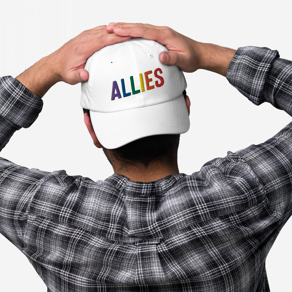 Person in plaid shirt holds a white Allies Rainbow Hat, featuring rainbow-colored embroidered letters, symbolizing support for LGBTQ+ rights and equality, aligning with a message of pride and activism.