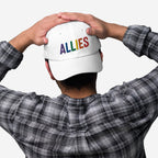 Person in plaid shirt holds a white Allies Rainbow Hat, featuring rainbow-colored embroidered letters, symbolizing support for LGBTQ+ rights and equality, aligning with a message of pride and activism.