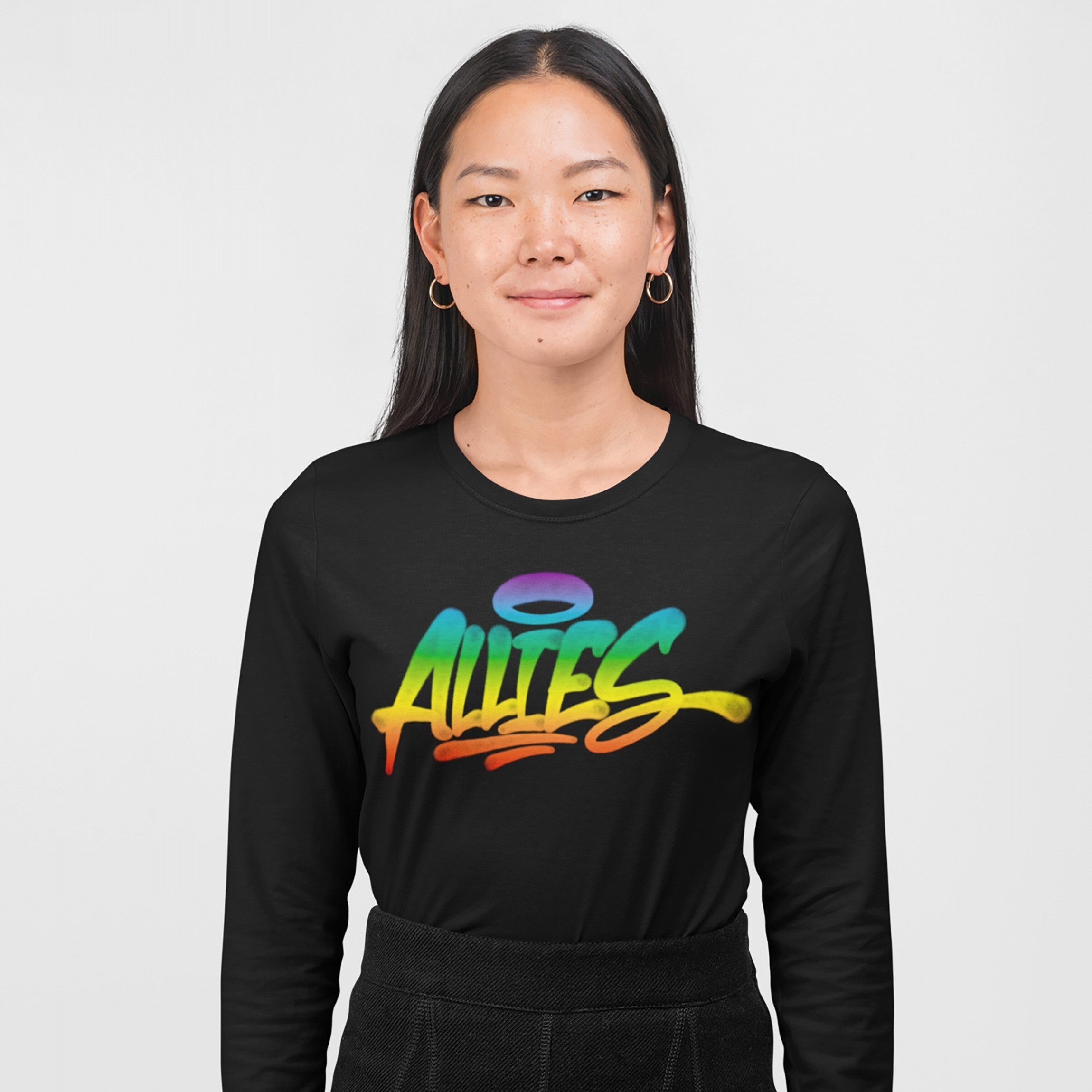 Woman wearing Allies Rainbow Handstyle T-shirt, featuring graffiti-style Allies text in rainbow gradient, paired with dark trousers and hoop earrings, symbolizing LGBTQ+ solidarity and inclusion.