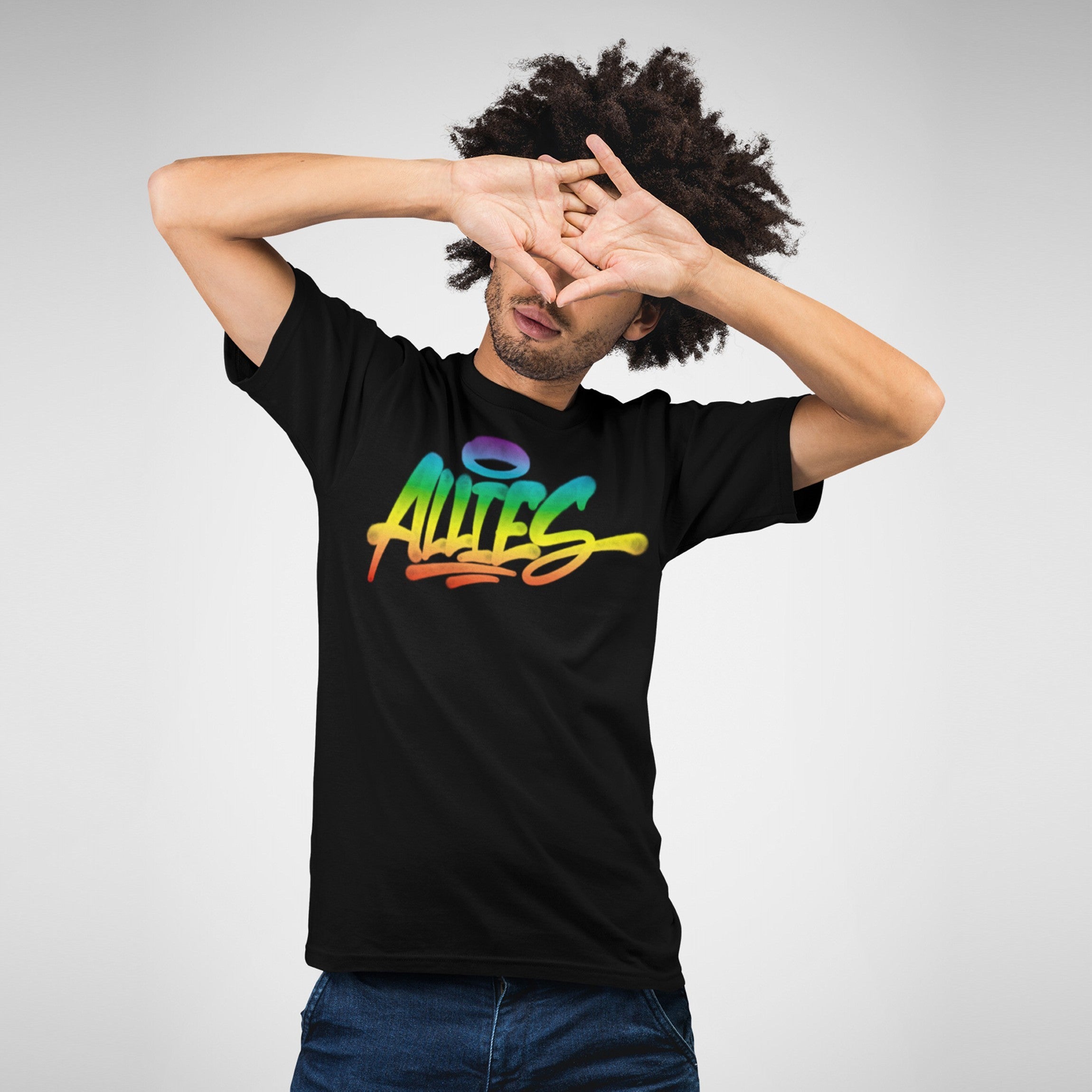 Person wearing the Allies Rainbow Handstyle T-shirt with “Allies” in graffiti-style rainbow gradient. Arms raised, partially obscuring face, against a plain light background, symbolizing LGBTQ+ solidarity and inclusivity.