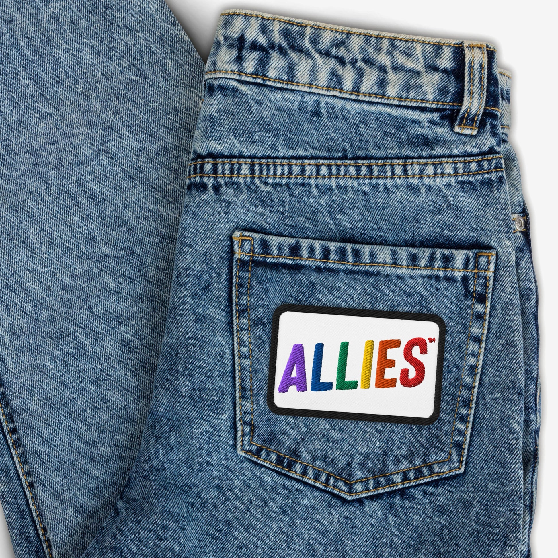 The Allies Rainbow Patch adorns the back pocket of blue denim jeans, featuring vibrant multicolored letters, symbolizing LGBTQ+ support and allyship.