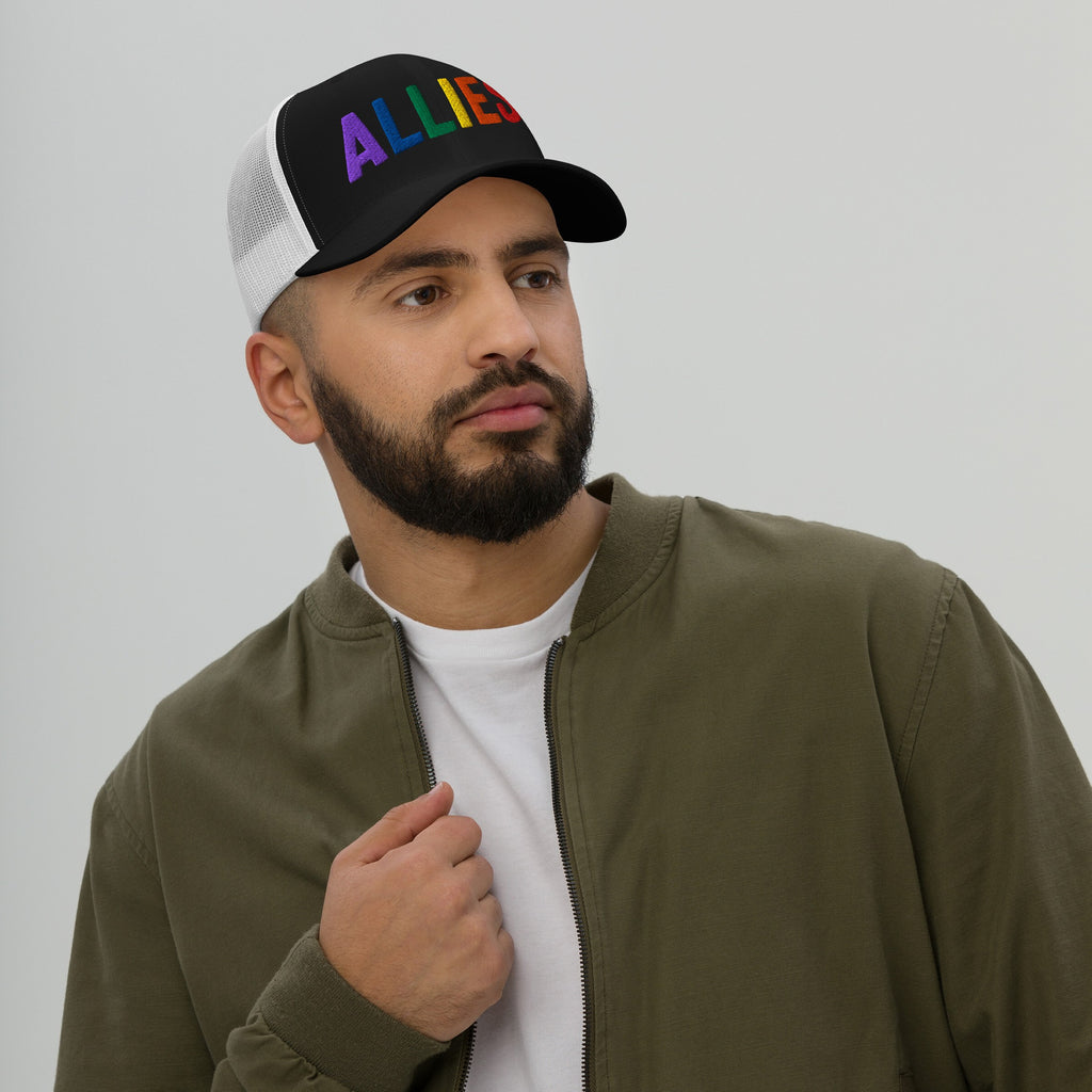 A bearded man models the Allies Rainbow Hat, featuring ALLIES in rainbow letters on a black-and-white mesh cap. Embrace LGBTQ+ support with this bold accessory for everyday solidarity.