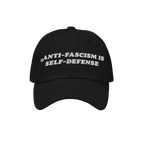 Black baseball-style cap with white embroidered text, “ANTI-FASCISM IS SELF-DEFENSE.” The Anti Fascism Is Self Defense Ha