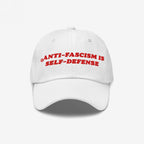 White unstructured baseball cap with bold red embroidery stating “ANTI-FASCISM IS SELF-DEFENSE.” Ideal for activists and allies, this hat supports the ACLU and champions human rights advocacy.