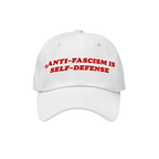 White unstructured baseball cap with bold red embroidery stating “ANTI-FASCISM IS SELF-DEFENSE.” Ideal for activists and 