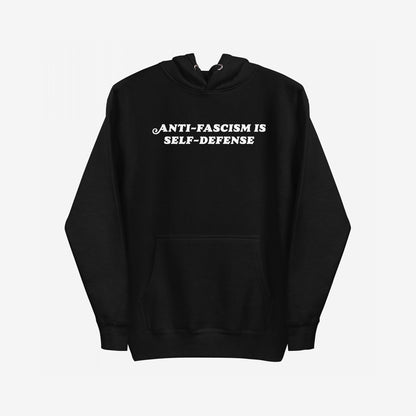 Black pullover Anti-Fascism Is Self-Defense Hoodie with a kangaroo pocket, featuring bold white text on the chest. Designed for those who stand against hate, it combines retro style with a powerful message.
