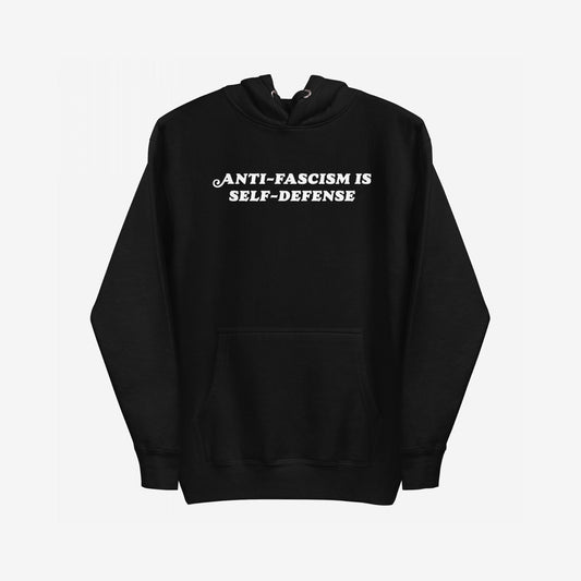 Black pullover Anti-Fascism Is Self-Defense Hoodie with a kangaroo pocket, featuring bold white text on the chest. Designed for those who stand against hate, it combines retro style with a powerful message.