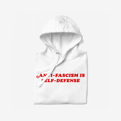 Anti-Fascism Is Self-Defense Hoodie, featuring bold red text on the front. The white hoodie is folded with its hood up and drawstring visible, embodying a strong, confrontational message.