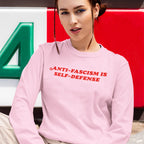 Young person in light pink Anti-Fascism Is Self-Defense sweatshirt, styled with braids and blue eyeliner, embodying activism and justice values for equality.
