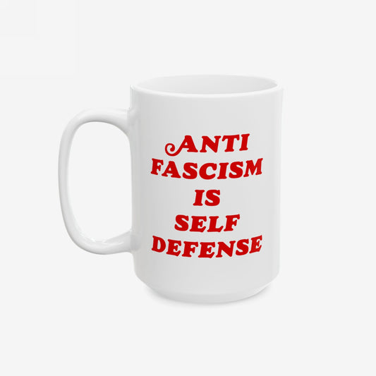 White ceramic Anti-Fascism Is Self-Defense mug with bold red lettering, featuring a standard C-handle. Perfect for expressing convictions against fascism while enjoying your favorite beverage. Available in 11 oz. and 15 oz. sizes.