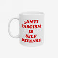 White ceramic mug with bold red text ANTI FASCISM IS SELF DEFENSE on the front, emphasizing strong political beliefs. Designed for those who oppose fascism, this mug supports ACLU donations.