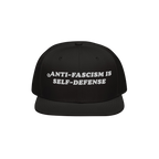 Black snap-back cap with the bold, white embroidered text ANTI-FASCISM IS SELF-DEFENSE, ideal for activists advocating human 