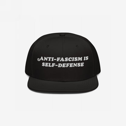 Black flat-brimmed snapback hat, “Anti-Fascism Is Self-Defense” embroidered boldly in white. A statement piece for those who resist.