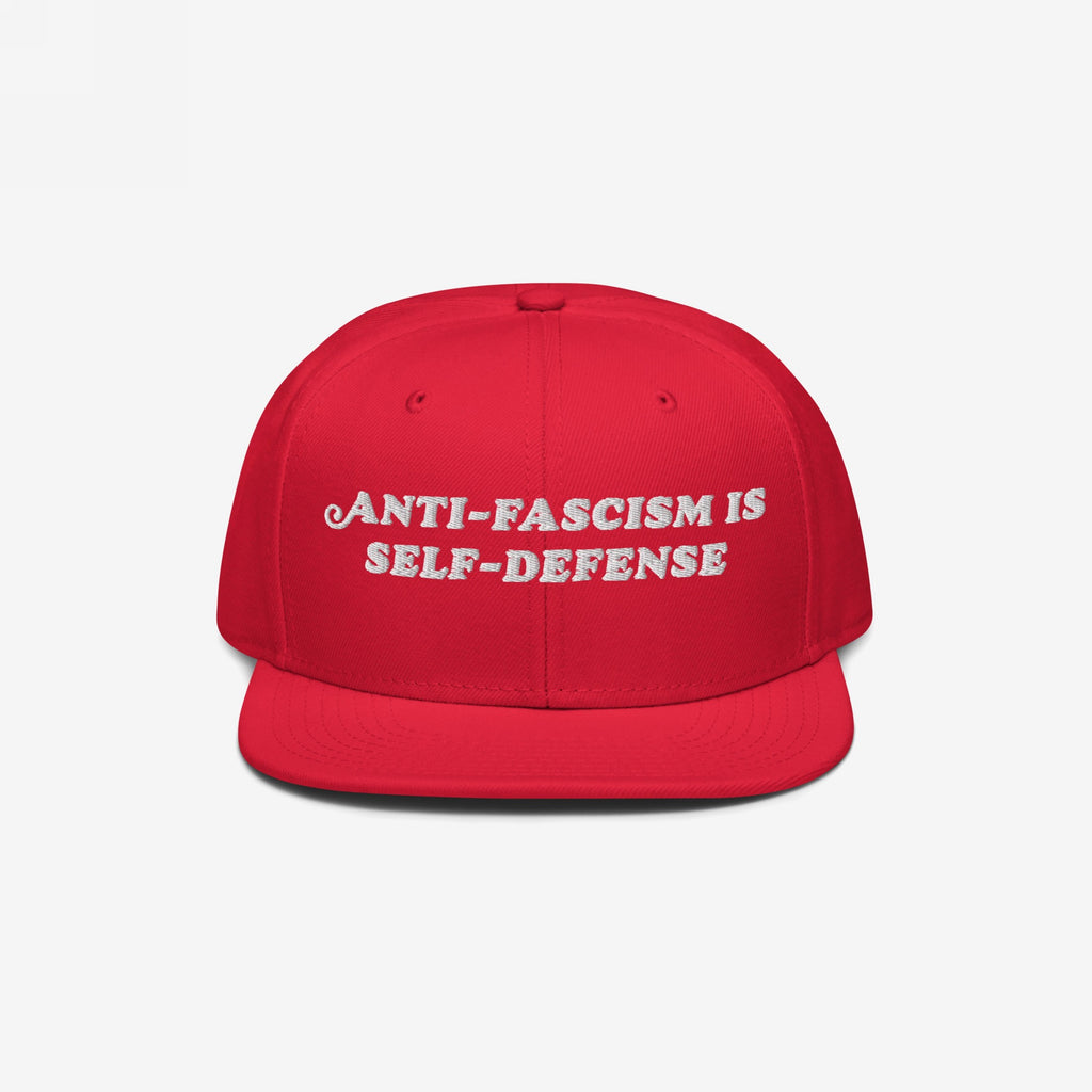 Bright red snapback cap with “ANTI-FASCISM IS SELF-DEFENSE” embroidered in white, embodying activist spirit. Ideal for rallies, supporting ACLU, and promoting equality.
