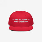 Bright red snapback cap with “ANTI-FASCISM IS SELF-DEFENSE” embroidered in white, embodying activist spirit. Ideal for rallies, supporting ACLU, and promoting equality.