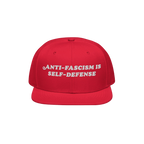 Bright red snapback cap with “ANTI-FASCISM IS SELF-DEFENSE” embroidered in white, embodying activist spirit. Ideal for ra