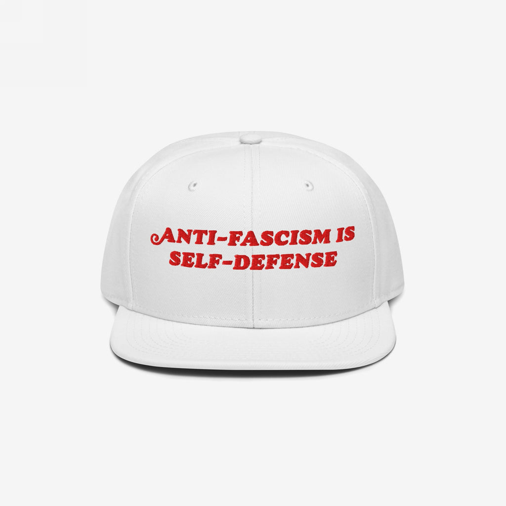 White flat-brimmed cap featuring bold red embroidery reading ANTI-FASCISM IS SELF-DEFENSE for activists and allies, embodying a vintage, unapologetic stance against fascism.
