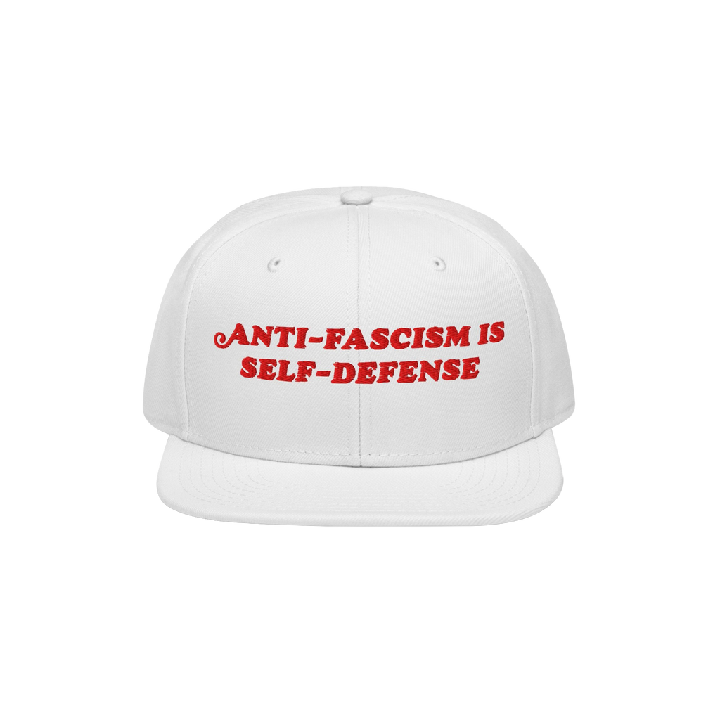 White flat-brimmed cap featuring bold red embroidery reading ANTI-FASCISM IS SELF-DEFENSE for activists and allies, embodying