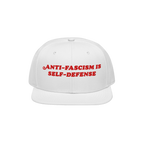 White flat-brimmed cap featuring bold red embroidery reading ANTI-FASCISM IS SELF-DEFENSE for activists and allies, embodying