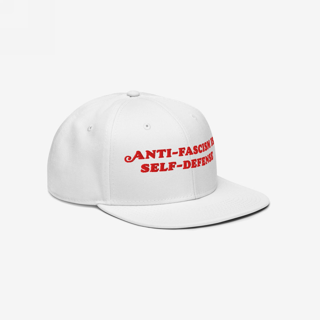 Anti Fascism Is Self Defense Hat features a bold slogan in red embroidery on a white baseball cap with a flat brim, embodying activist spirit and commitment to human rights.