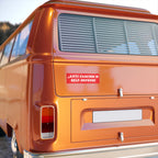 Rear view of an orange vintage-style van featuring an Anti-Fascism Is Self-Defense bumper sticker. The sticker, in red-and-white, emphasizes bold, clear messaging against fascism for vehicle display.
