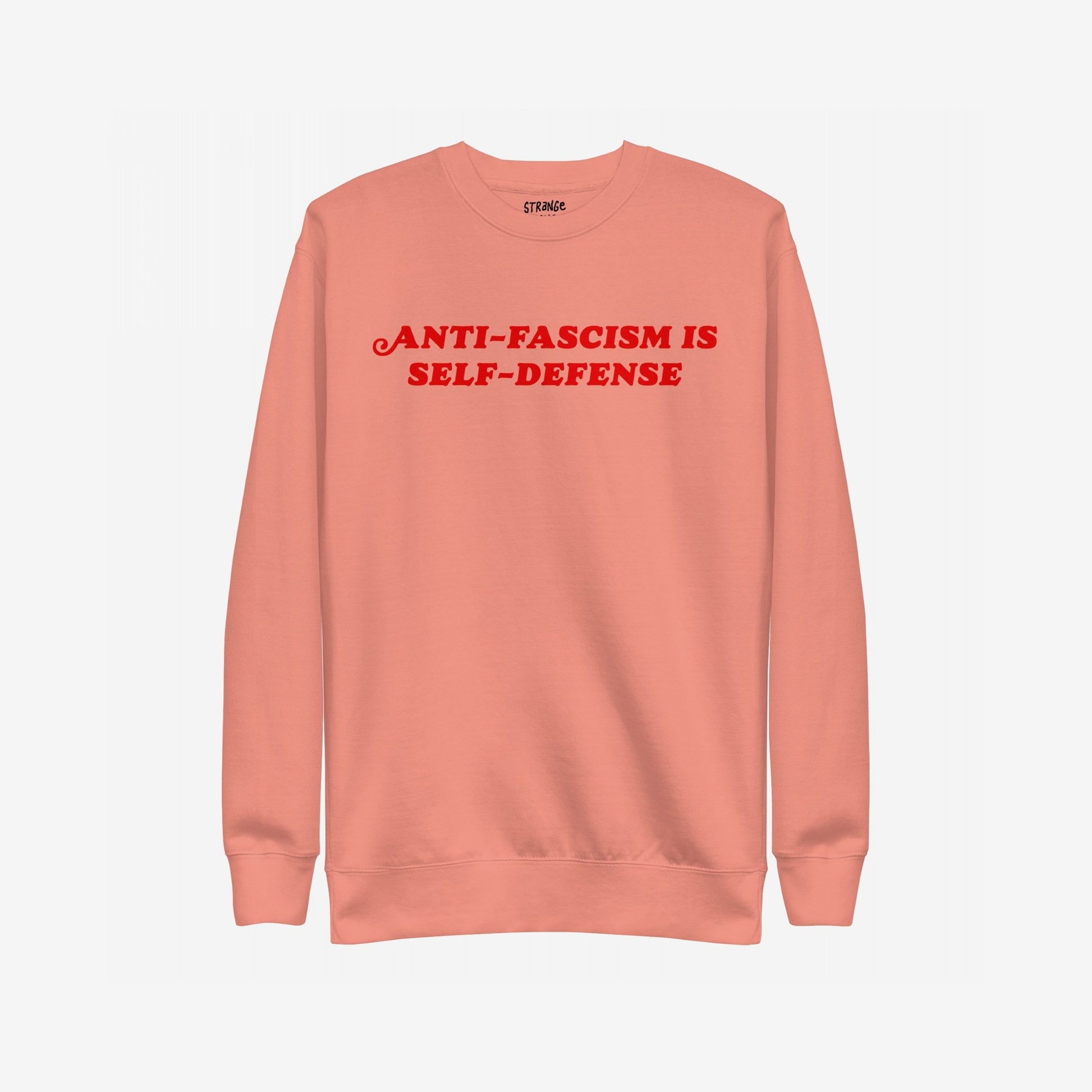 Coral-pink crewneck sweatshirt with bold red ANTI-FASCISM IS SELF-DEFENSE text across the chest, embodying the Anti-Fascism Is Self-Defense Hoodie & Sweatshirt's message of resistance and solidarity.