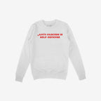 A plain white crewneck sweatshirt with bold red text reading “ANTI-FASCISM IS SELF-DEFENSE,” embodying activism and style.