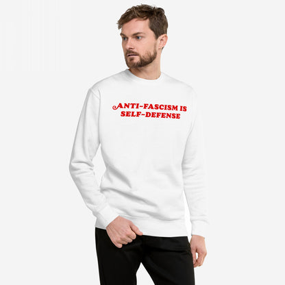 Model wearing Anti-Fascism Is Self-Defense Hoodie & Sweatshirt with bold red slogan, embodying a message of resistance and equality, standing against a plain backdrop.