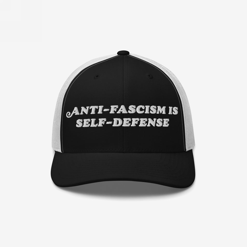 Two-tone trucker-style baseball cap with embroidered slogan “ANTI-FASCISM IS SELF-DEFENSE” on the front, embodying activist spirit and designed for those who stand against fascism in style.