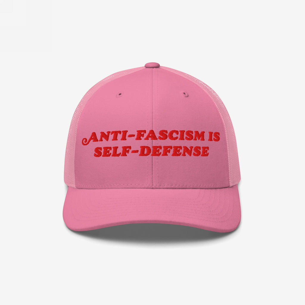 Pink trucker-style baseball cap with red embroidered “ANTI-FASCISM IS SELF-DEFENSE” text, embodying activist spirit. Ideal for allies and organizers committed to human rights and resisting fascism through fashion.