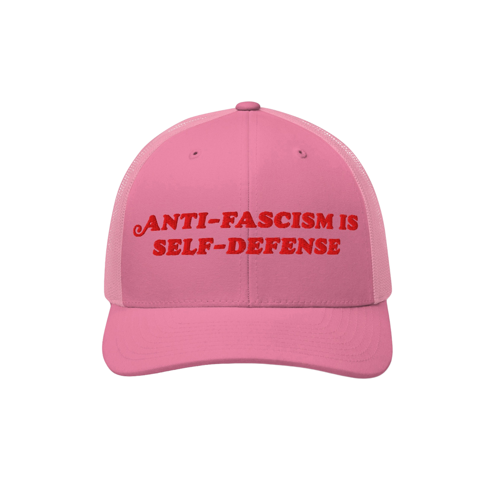 Pink trucker-style baseball cap with red embroidered “ANTI-FASCISM IS SELF-DEFENSE” text, embodying activist spirit. Idea
