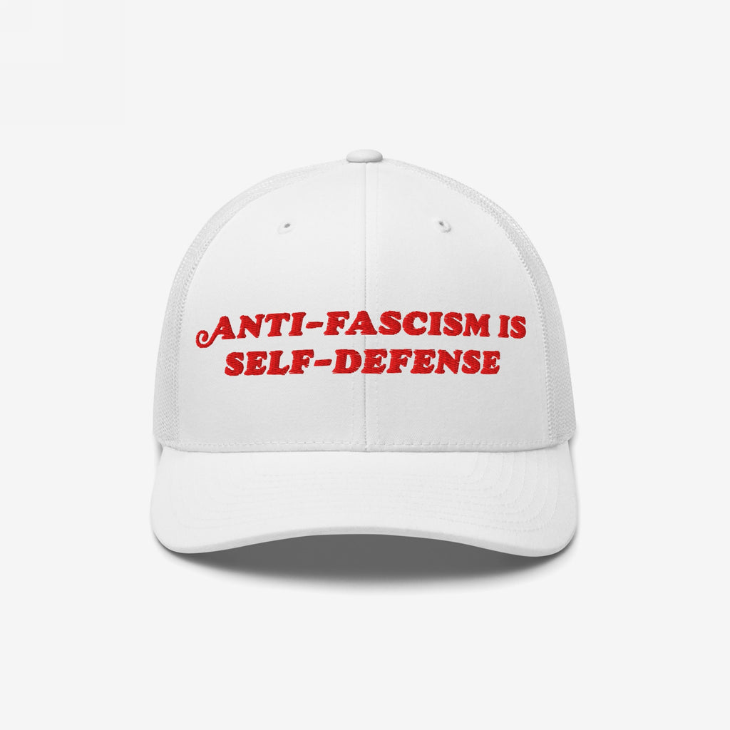 White mesh-back trucker hat with bold red embroidery reading “ANTI-FASCISM IS SELF-DEFENSE,” embodying activism and resistance. Ideal for allies and advocates, supporting ACLU's mission against fascism.