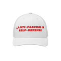 White mesh-back trucker hat with bold red embroidery reading “ANTI-FASCISM IS SELF-DEFENSE,” embodying activism and resis