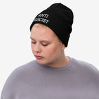 Person with light-blonde hair wears the Anti-Fascist Classic Hat, a black knit beanie with “ANTI FASCIST” in white. They look down, embodying a bold, resistance-driven style.