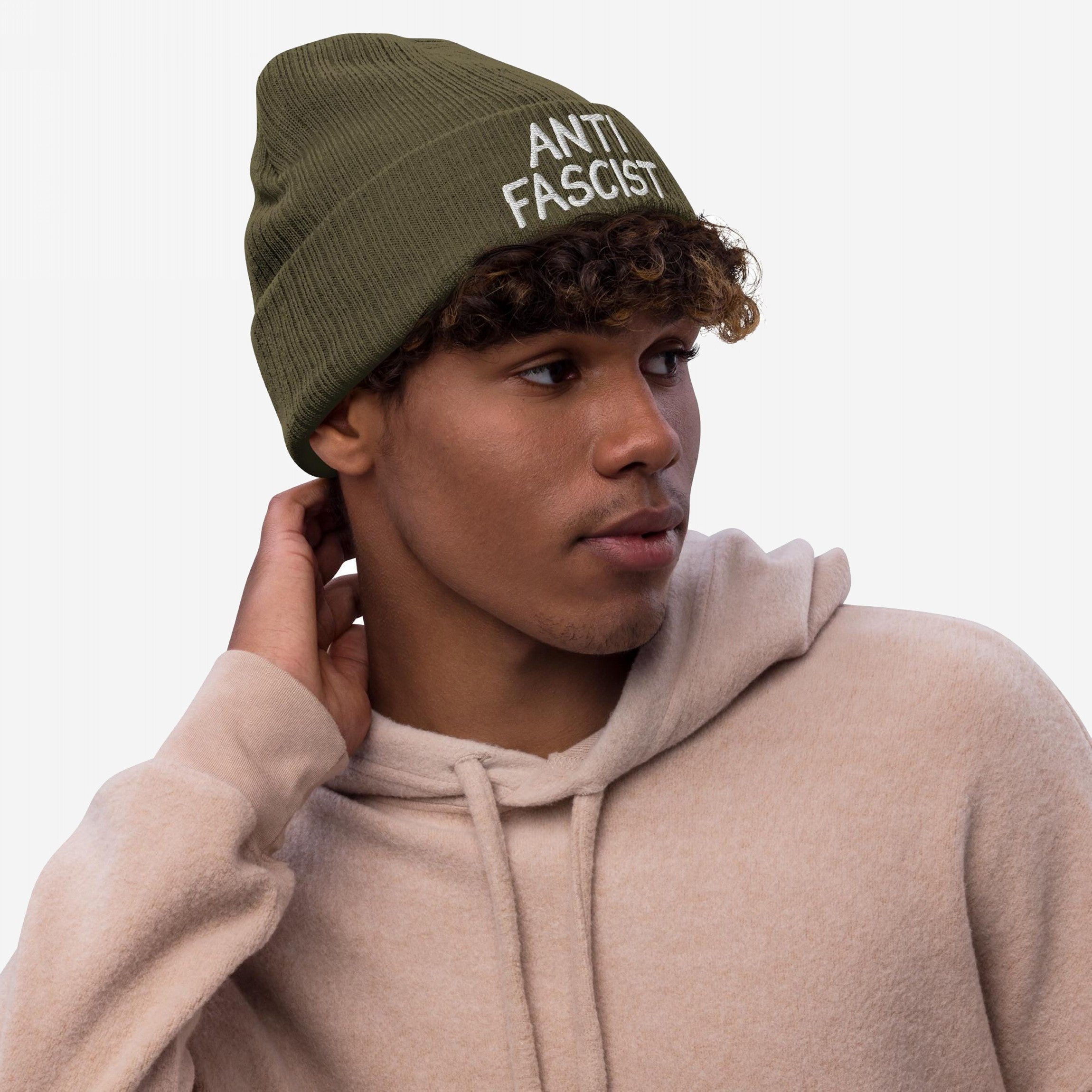Young person wearing the Anti Fascist Hat, an olive-green beanie with ANTI FASCIST embroidered in white, paired with a tan hoodie. A statement piece for those advocating against fascism.