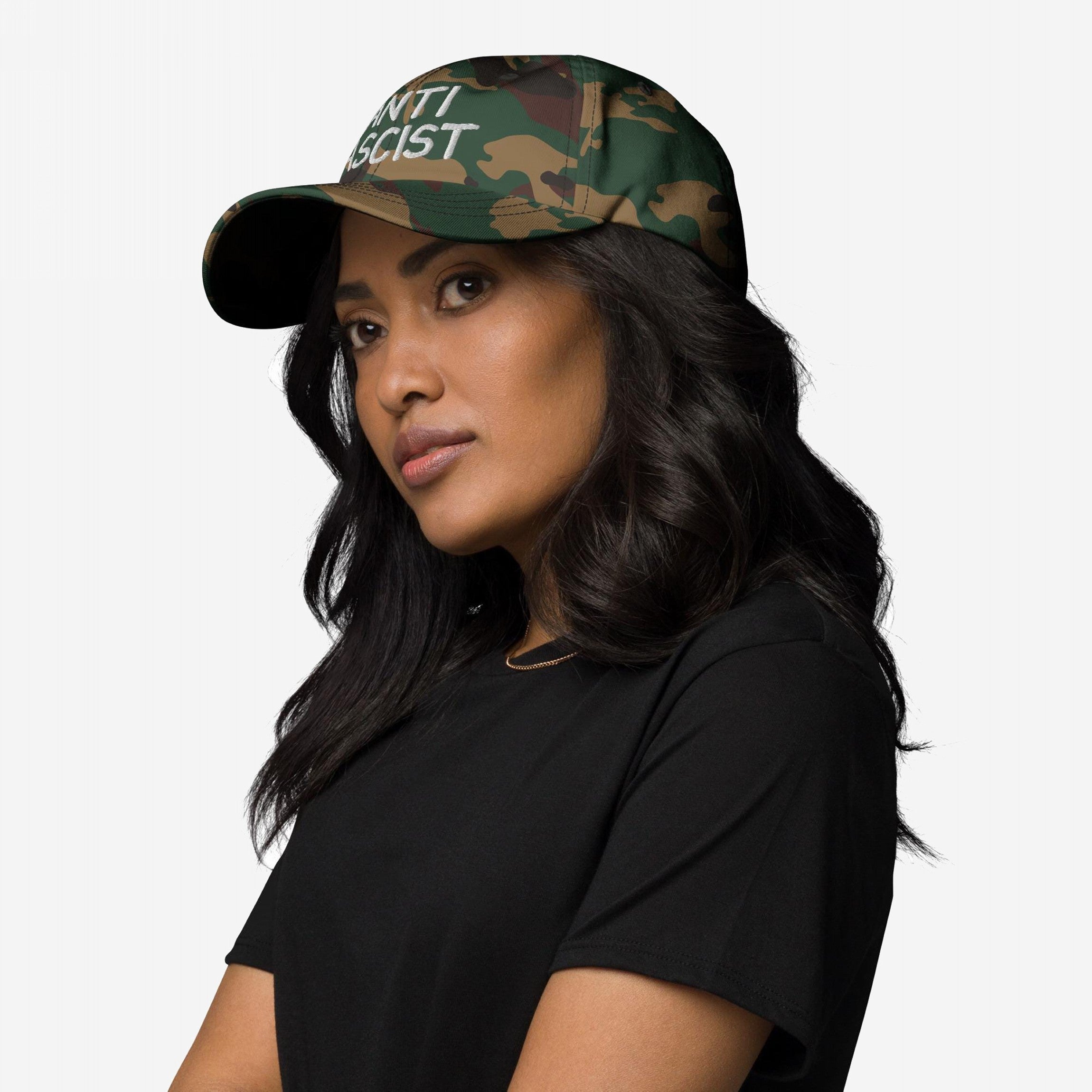A person wears the Anti Fascist Hat, featuring a camouflage pattern and ANTI FASCIST text, highlighting its bold stance. They pair it with a simple black T-shirt, embodying a message of resistance.