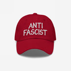 Anti Fascist Hat featuring ANTI FASCIST in white hand-drawn embroidery on a red baseball-style cap, embodying a stylish stand against fascism with everyday comfort and ethically made design.