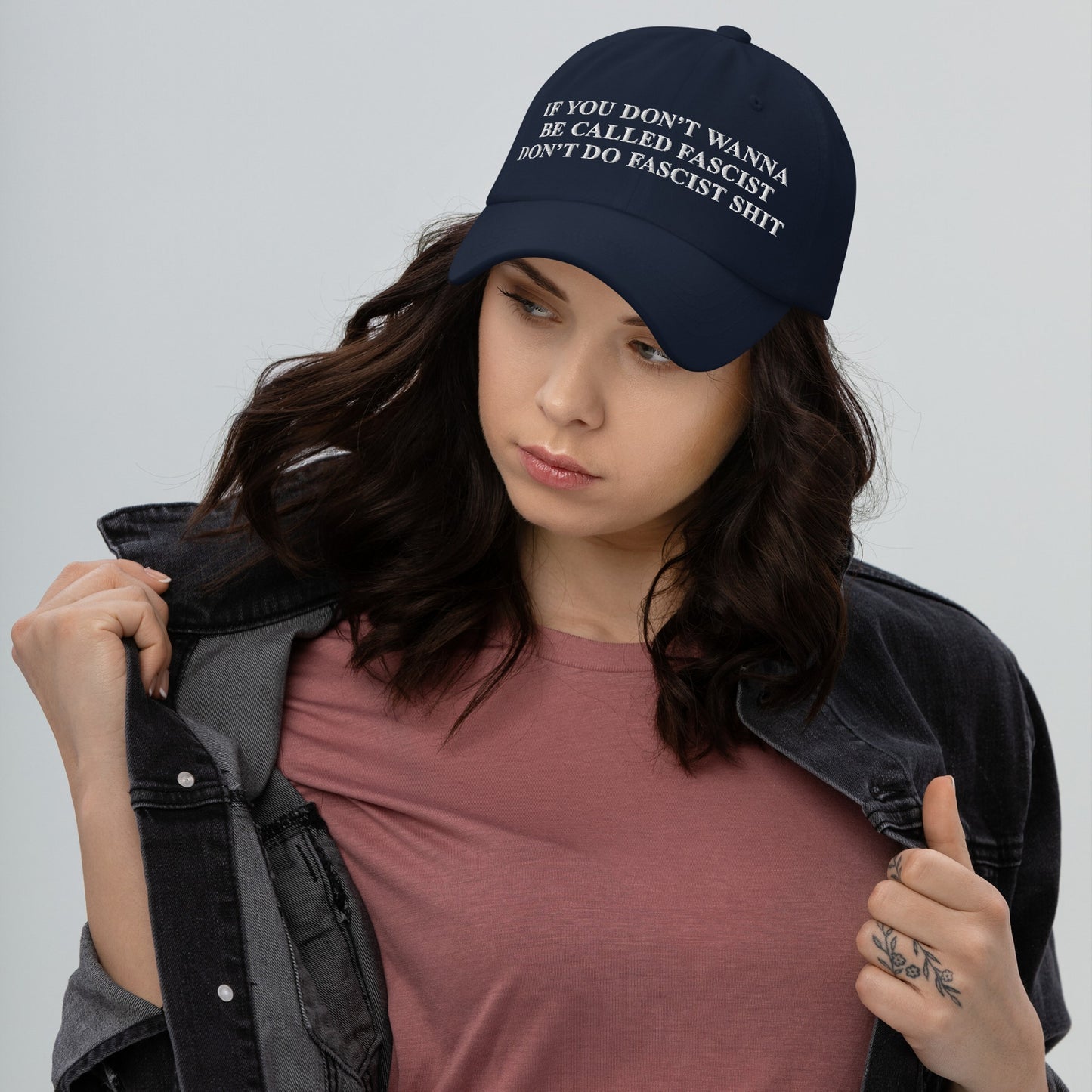 Young woman wearing the Anti-Fascist Retro Hat with bold embroidered text, styled with a dark denim jacket and rose-pink T-shirt, embodying a strong stance against fascism.