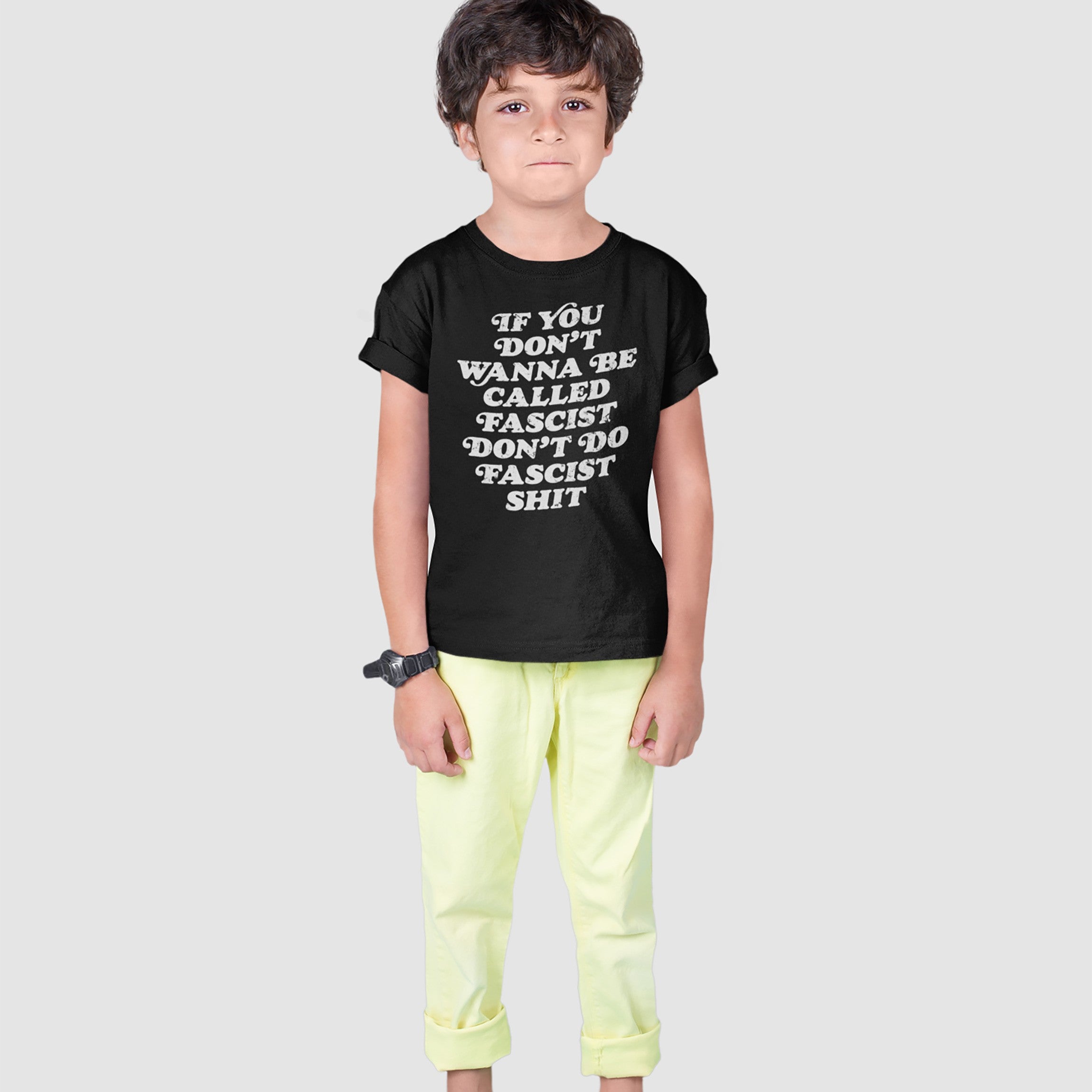 Young boy models the Anti-Fascist Retro Shirt, featuring bold white lettering with a strong anti-fascist message, paired with light rolled-up pants and a watch, embodying resistance and empowerment.
