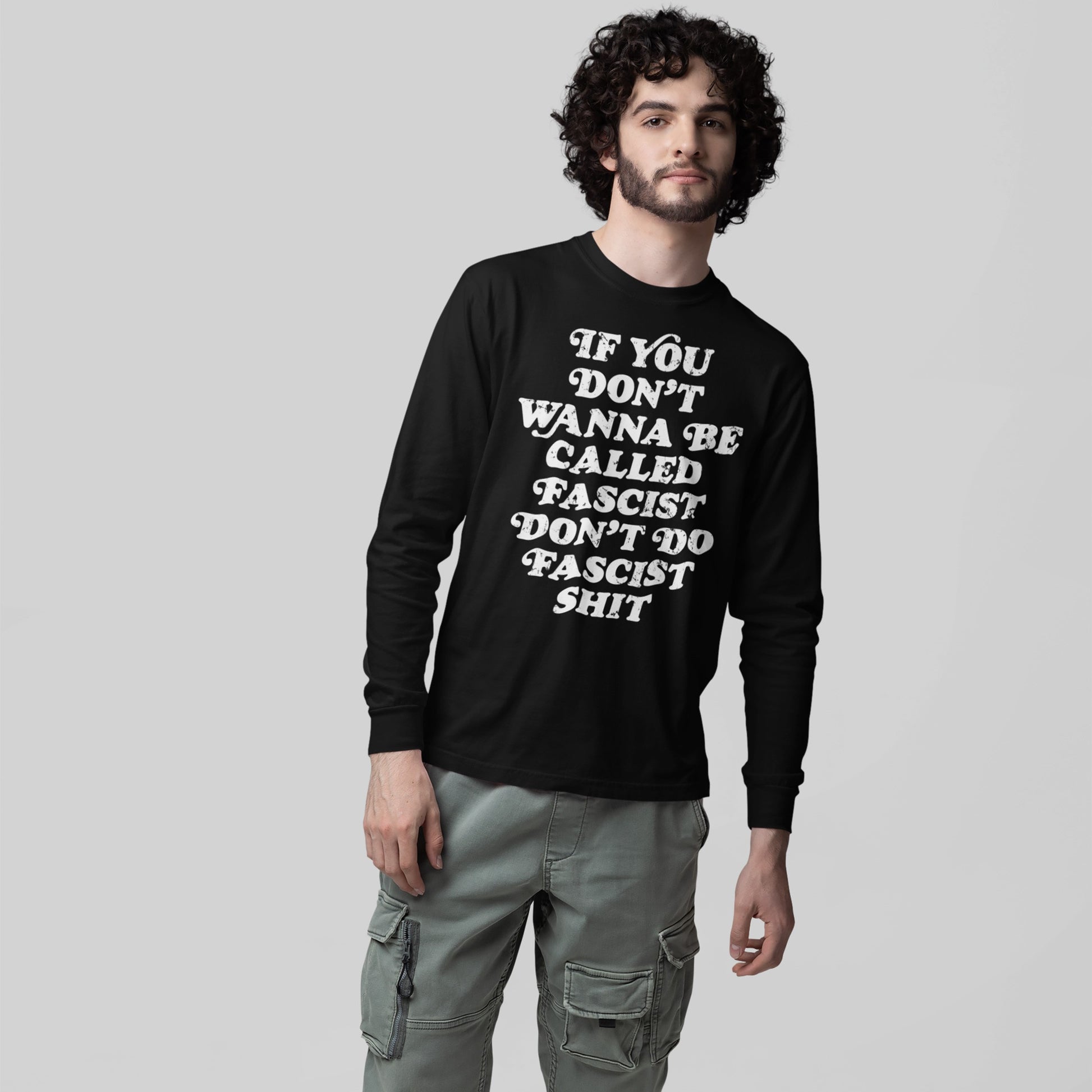 Young man wears the Anti-Fascist Retro Shirt, a black long-sleeve T-shirt with a bold message. Paired with olive-green cargo pants, it embodies a strong anti-fascist statement.