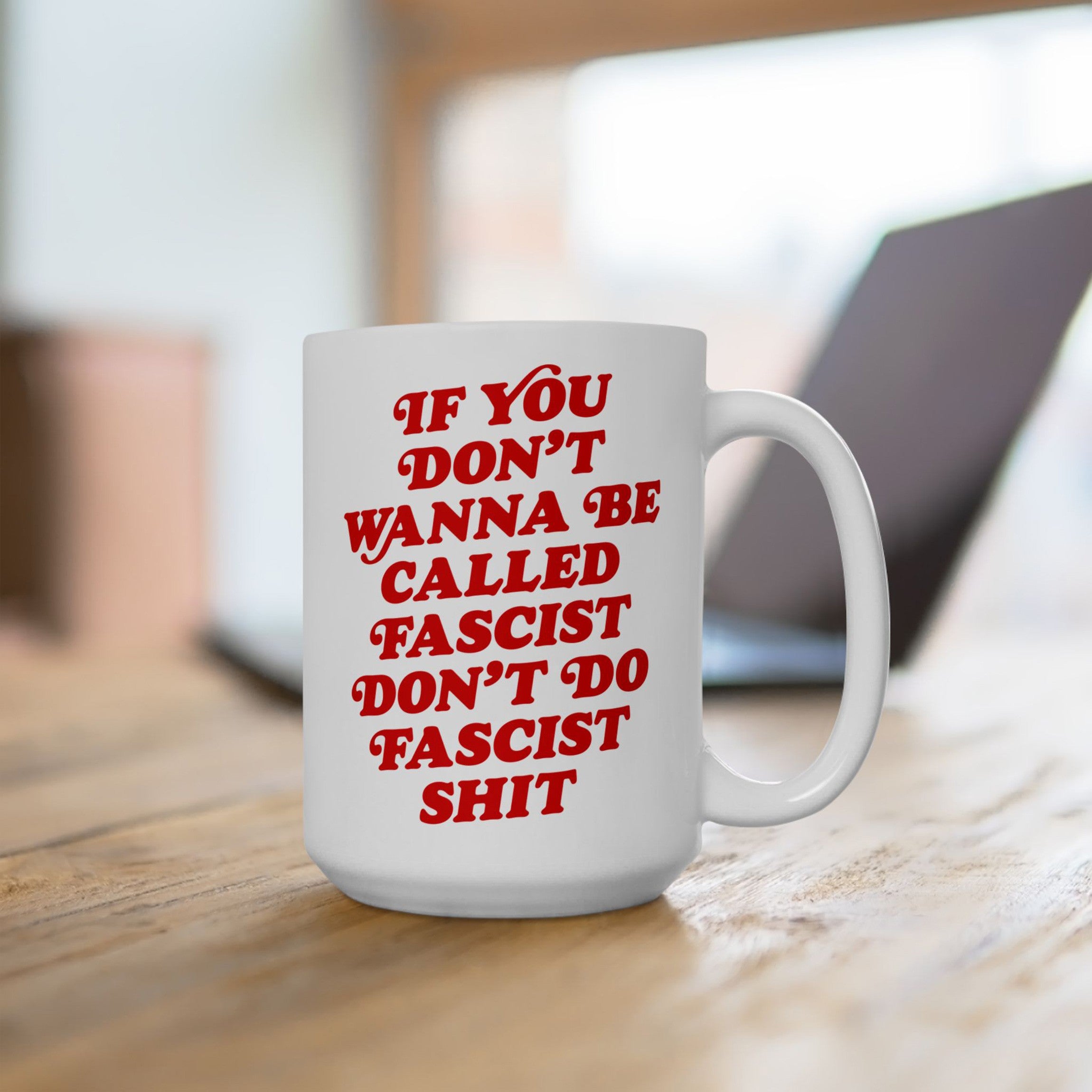 Anti-Fascist Retro Mug on wooden table, featuring bold red lettering with a strong message against fascism. Ideal for coffee or tea, symbolizing resistance and equality, with laptop blurred in background.