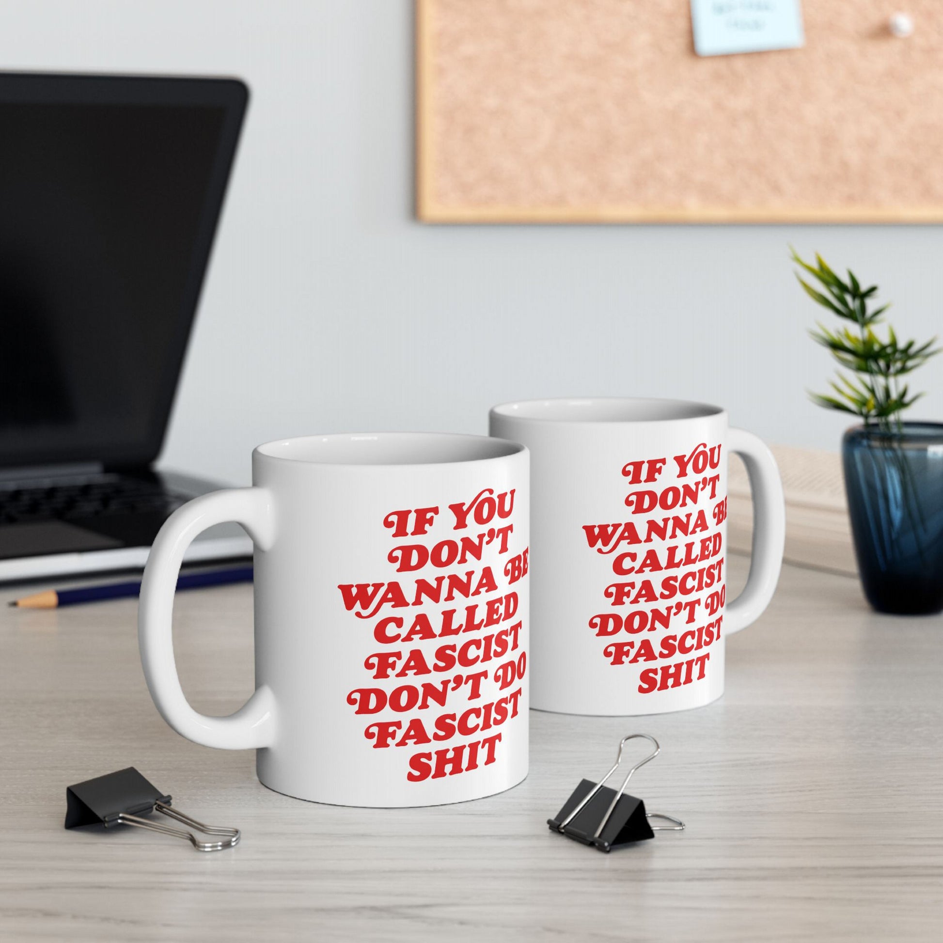 Anti-Fascist Retro Mug: Two white ceramic mugs with bold red text deliver a powerful message against fascism, set on a tidy desk with a laptop, pencil, and potted plant.