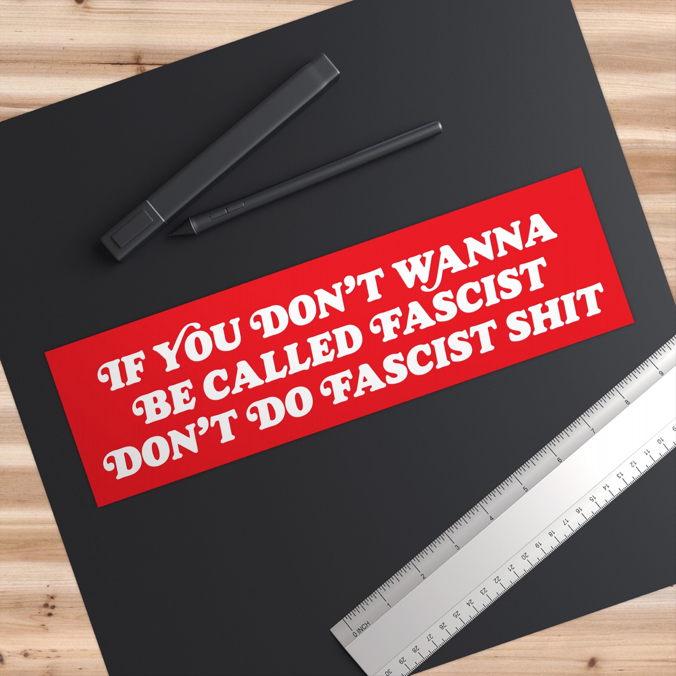Anti-Fascist Retro Sticker & Magnet on a wooden desk with digital-pen styluses and a ruler, showcasing bold text for displaying anti-fascist messages on cars, laptops, or fridges.