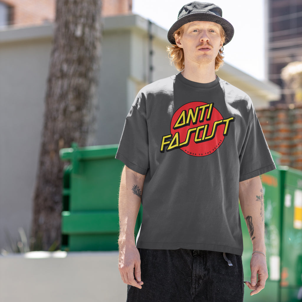 Young man wearing the Anti Fascist Shirt, featuring a bold red circle and Power to the People slogan, embodying skate style and progressive resistance against oppression, standing in an alley.